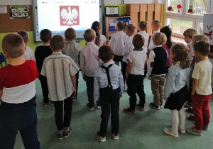 Dzieci stoją przed tablicą multimedialną oglądają prezentację pt. "Symbole Narodowe"